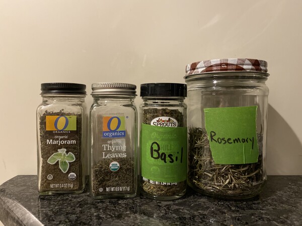 Four labelled spice jars. The marjoram and basil are full; thyme is about 1/3 full, and the rosemary is in large jar and half full.